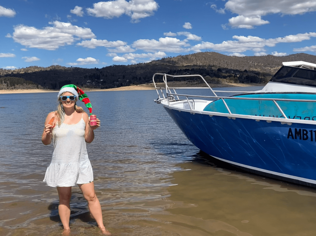Standing in the water next to a blue boat holding a prawn in one hand and a ginger beer in the other